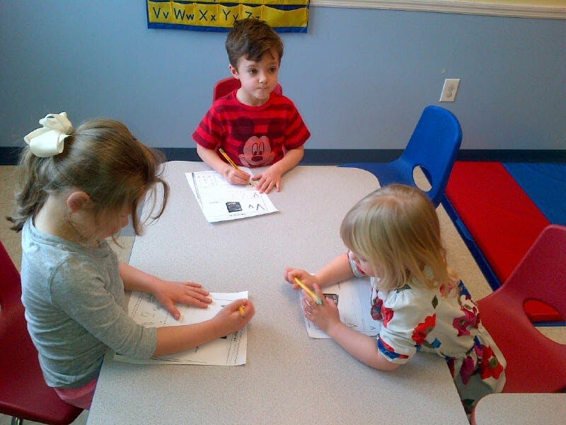 Three children drawing at a table in a classroom