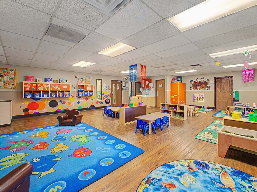 Classroom with colorful rugs, small tables and chairs, and bright wall decorations