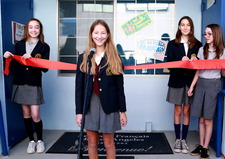 Four teens in school uniforms holding a red ribbon for a ceremony