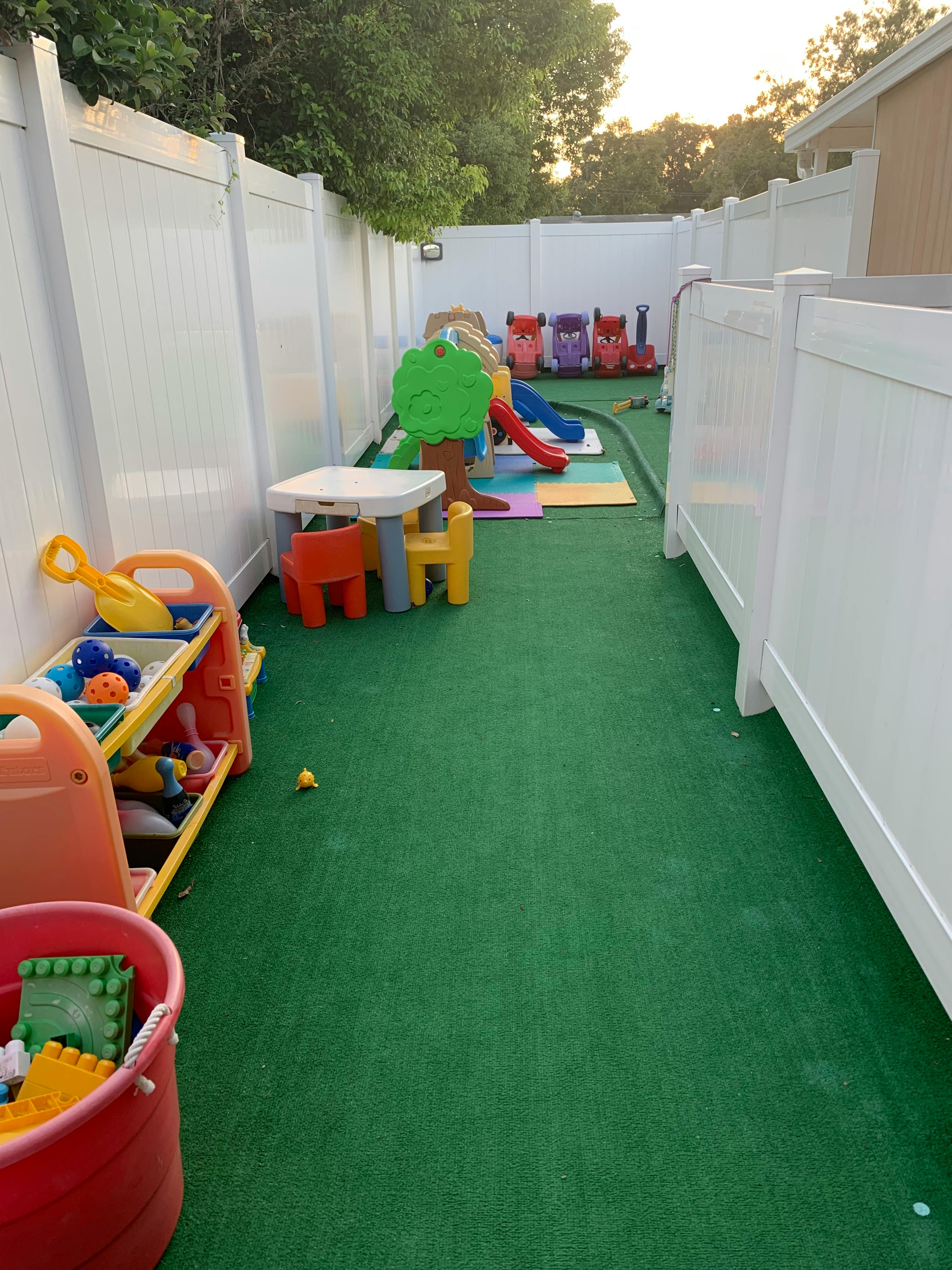 Outdoor play area with green turf, white fences, and colorful play equipment