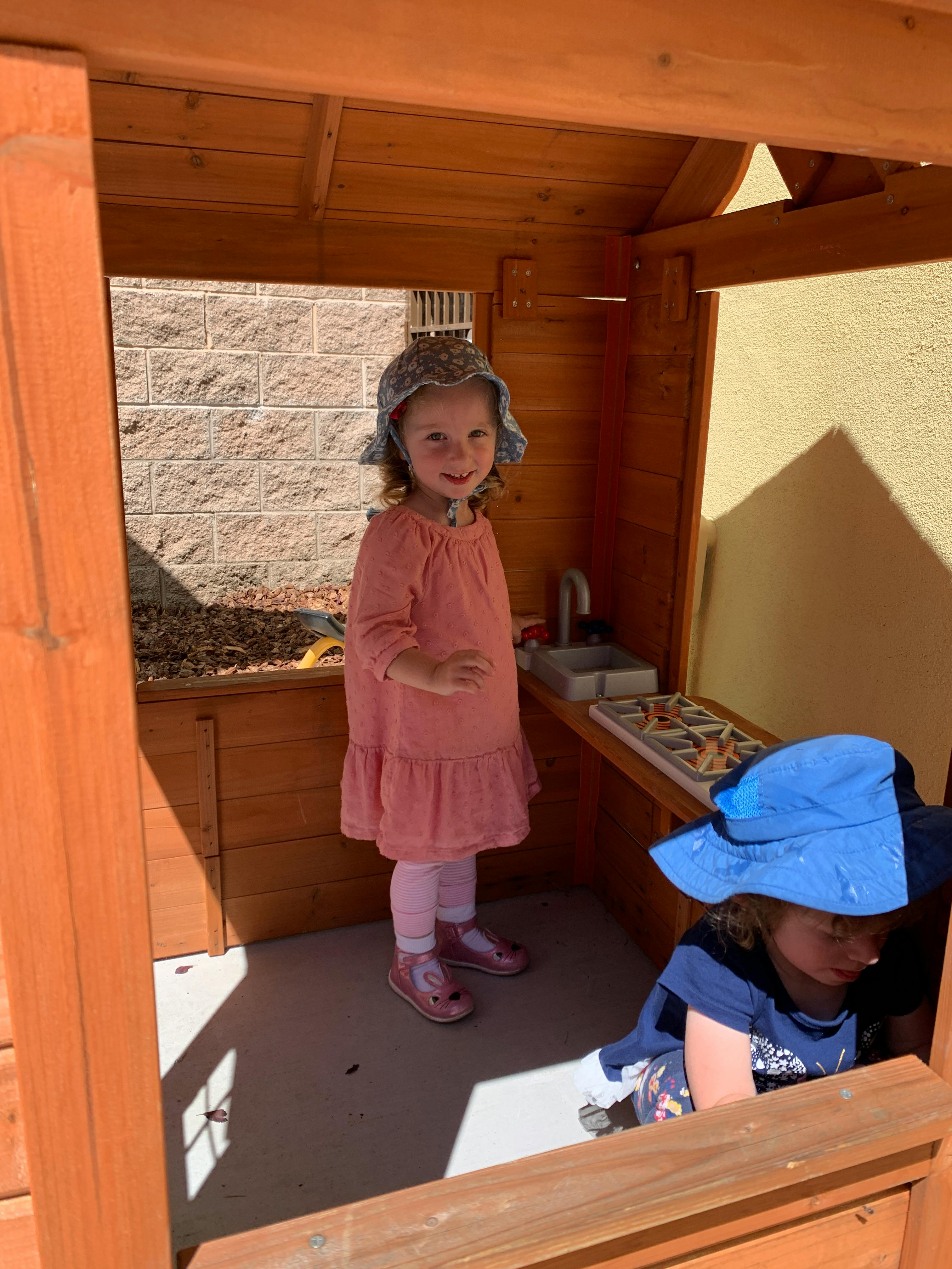Child in a playhouse with another child partially visible