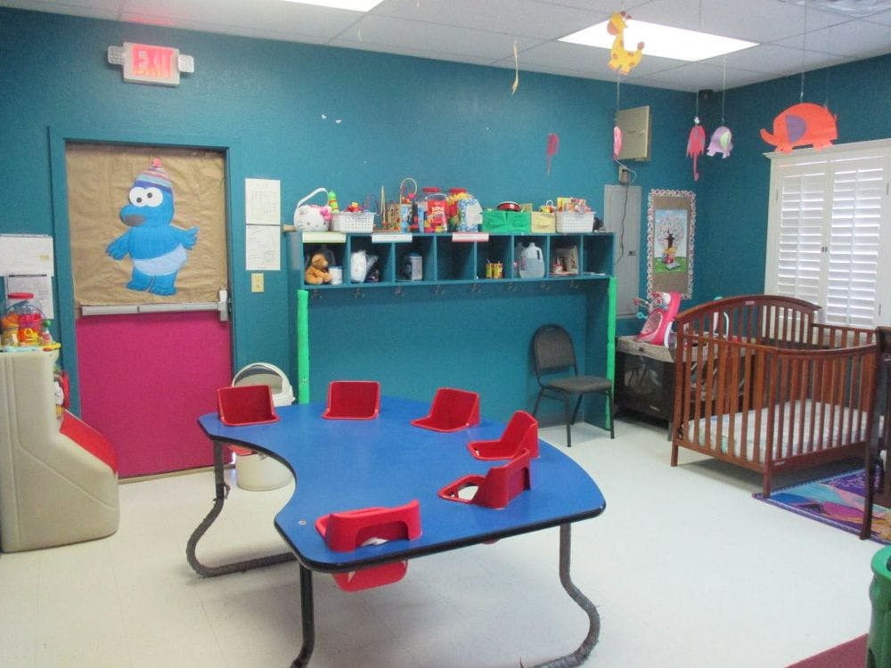 Children's playroom with a blue table and red chairs, shelves, and a crib