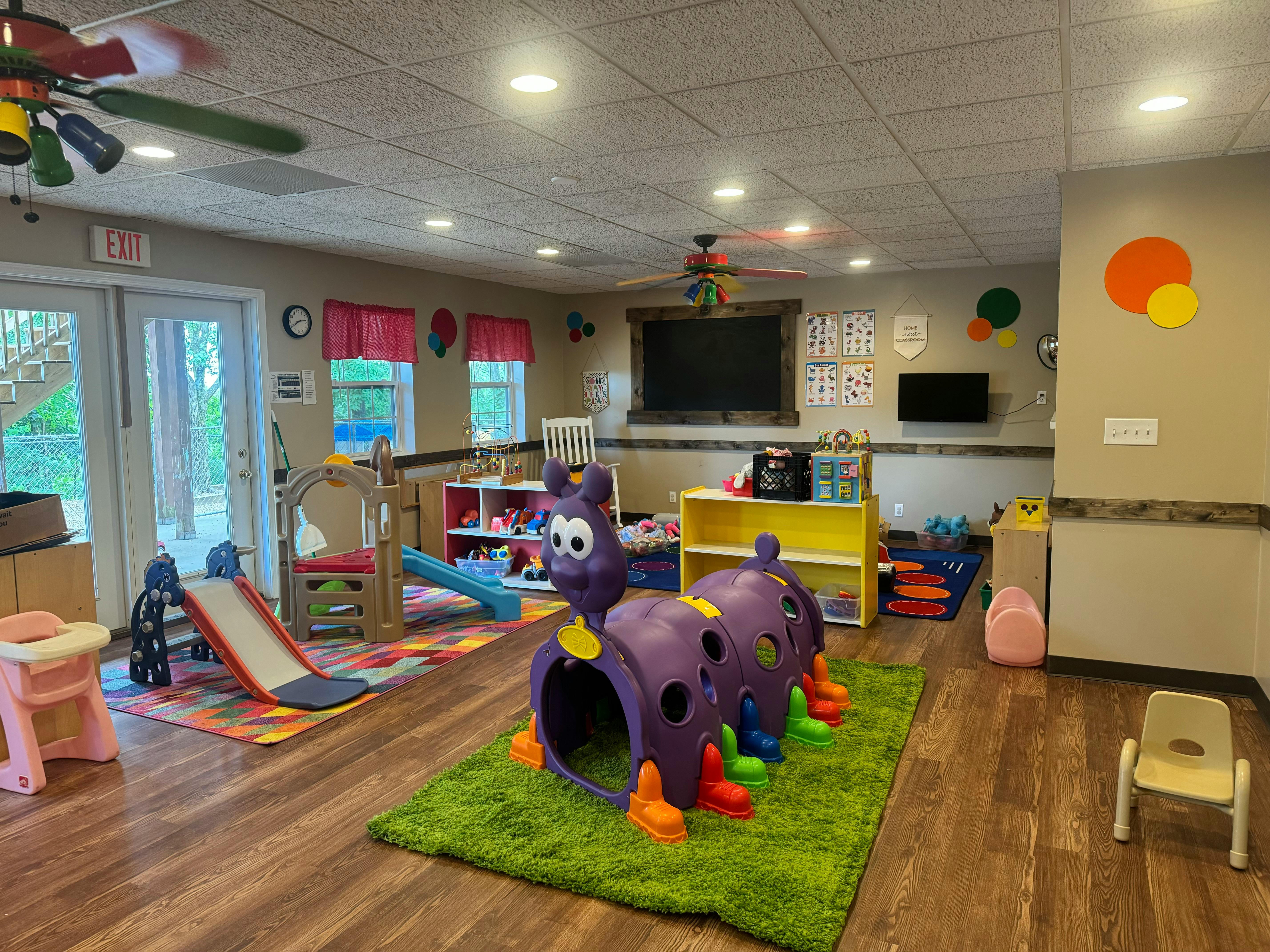 Indoor play area with a purple caterpillar tunnel, slide, and small chairs