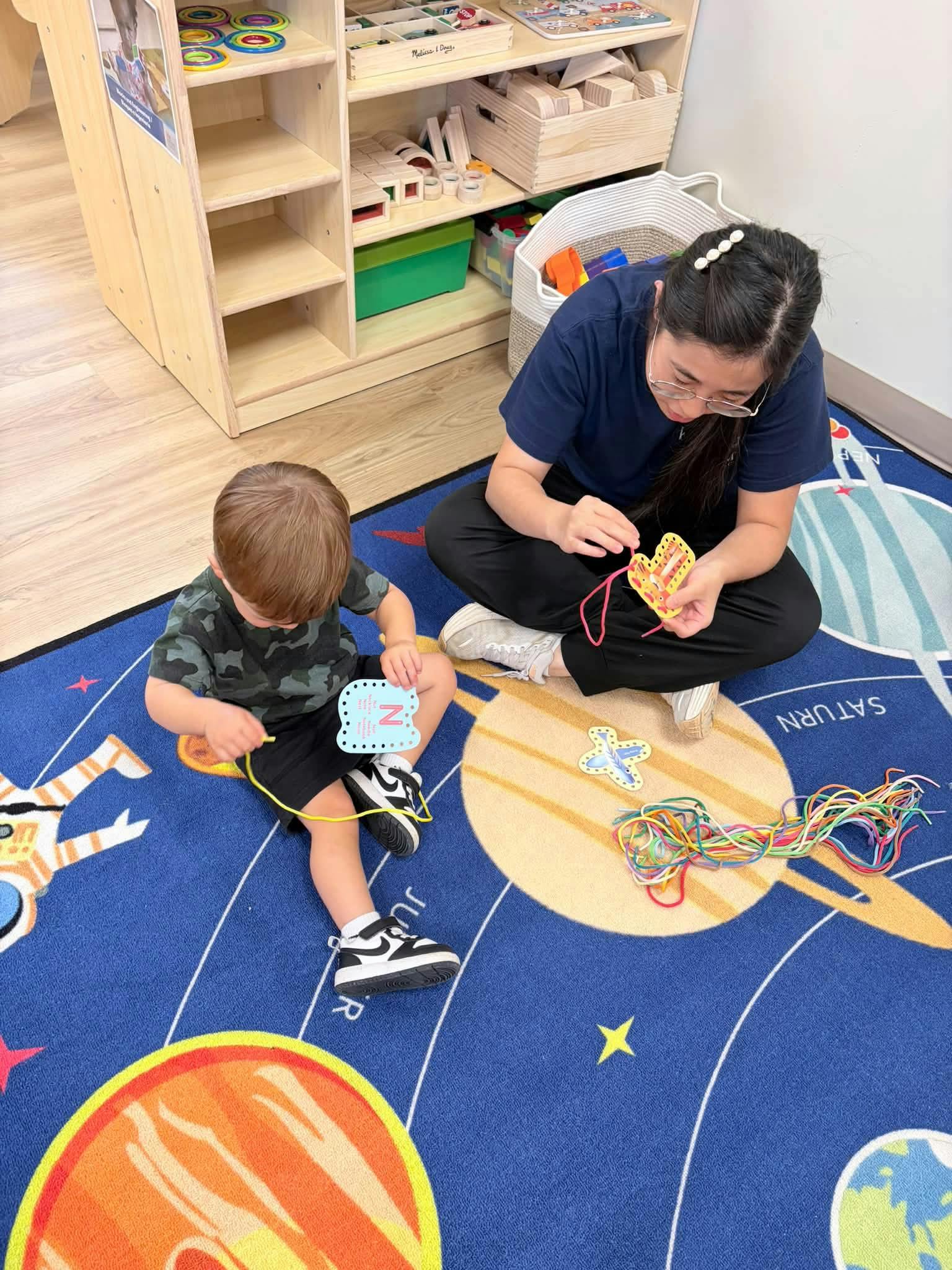 A person and a child sitting on a rug threading laces through shapes