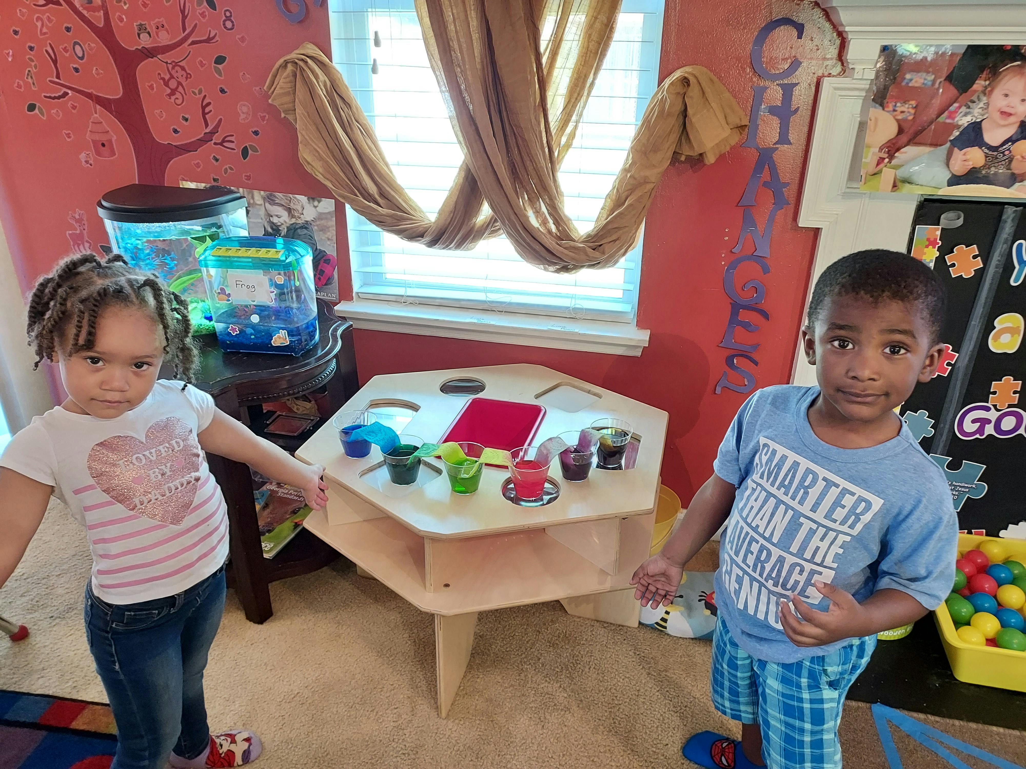 Two children standing in a room with a small table