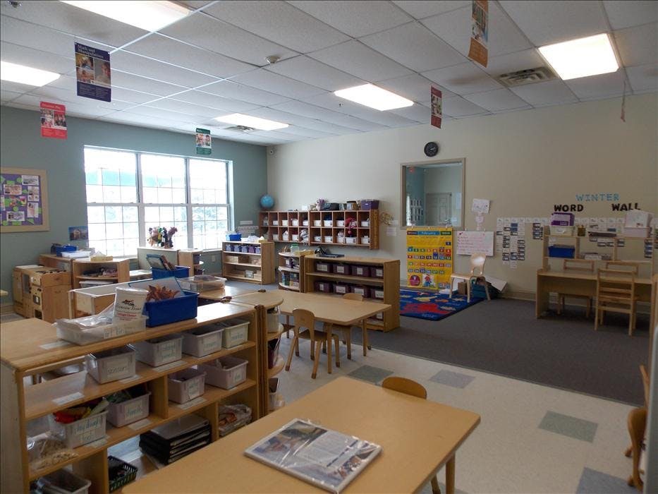 A brightly lit classroom with tables, chairs, and shelves of learning materials