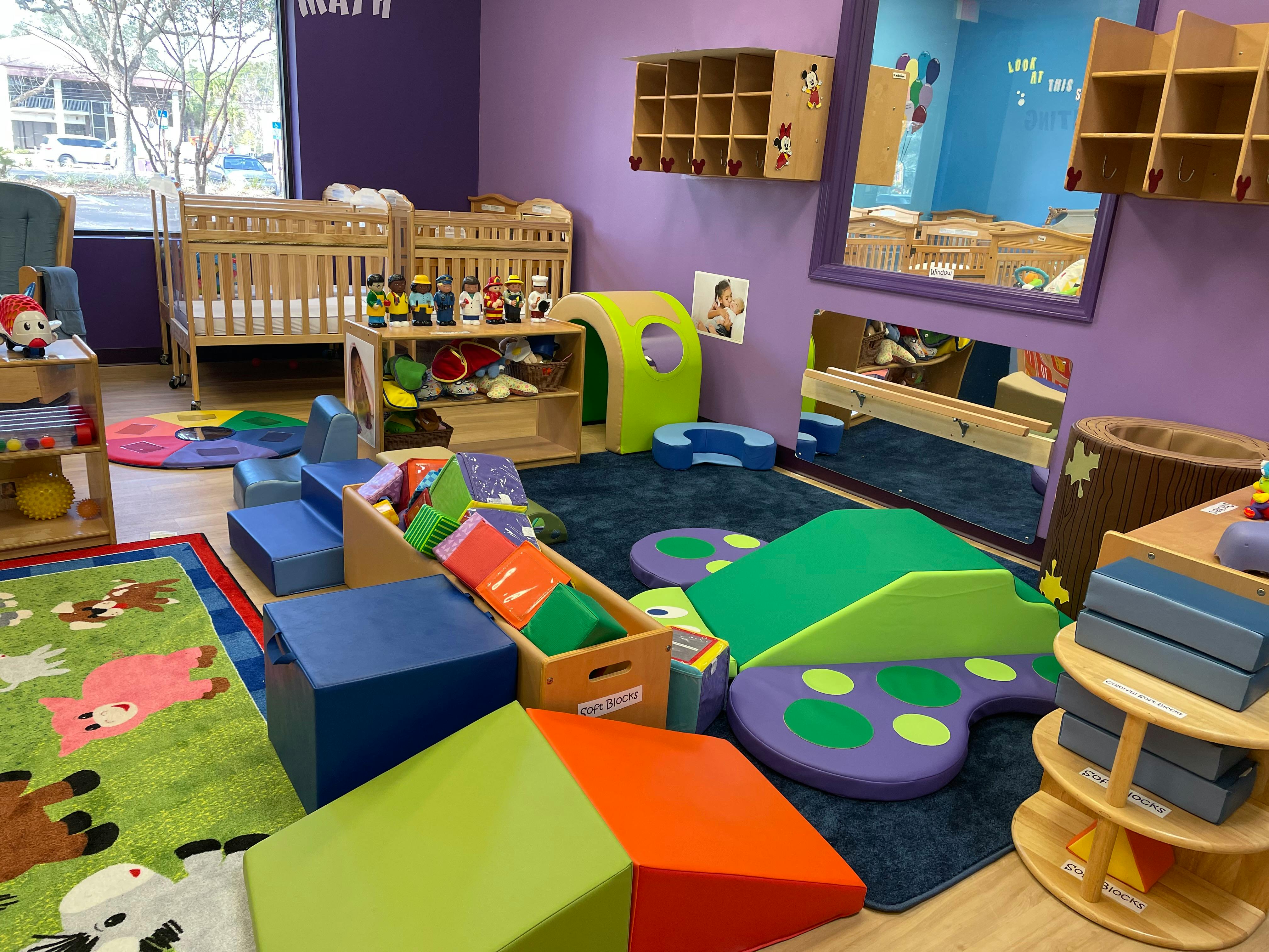 Baby room with cribs, soft play equipment, colorful rugs, and developmental toys
