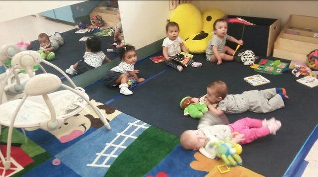 Multiple babies and children playing on a colorful rug with toys