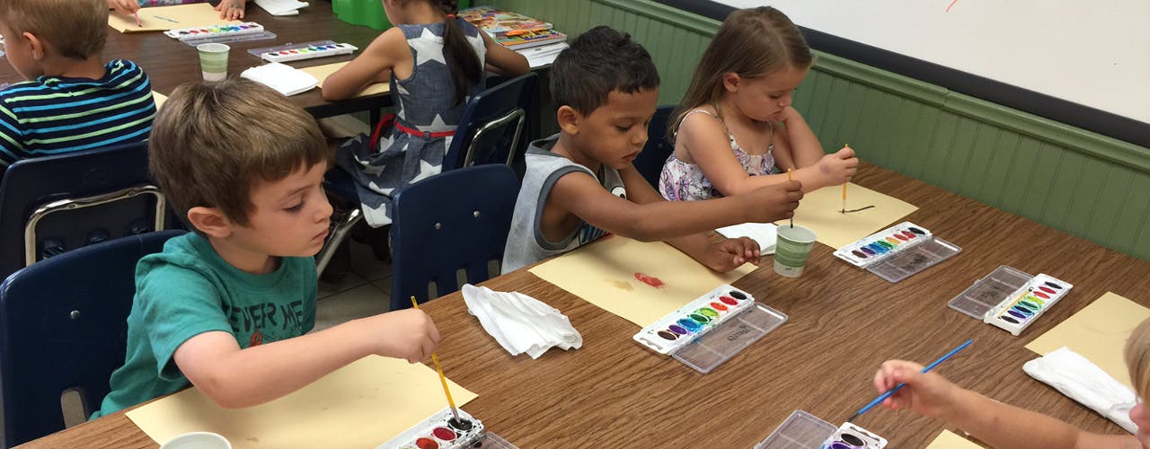 Children painting at a table in a classroom
