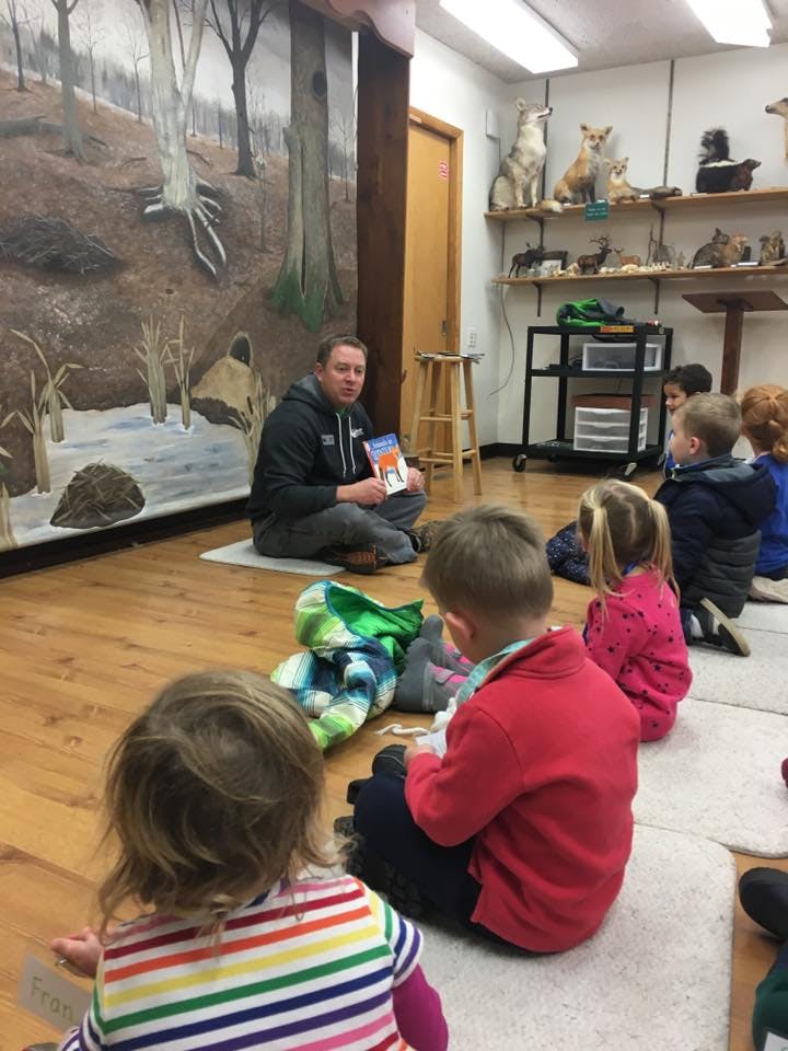 Person reading a book to a group of children sitting on the floor