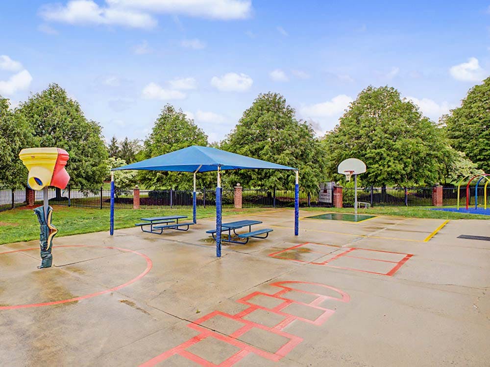Outdoor playground with basketball hoop, picnic tables under a canopy, and painted games