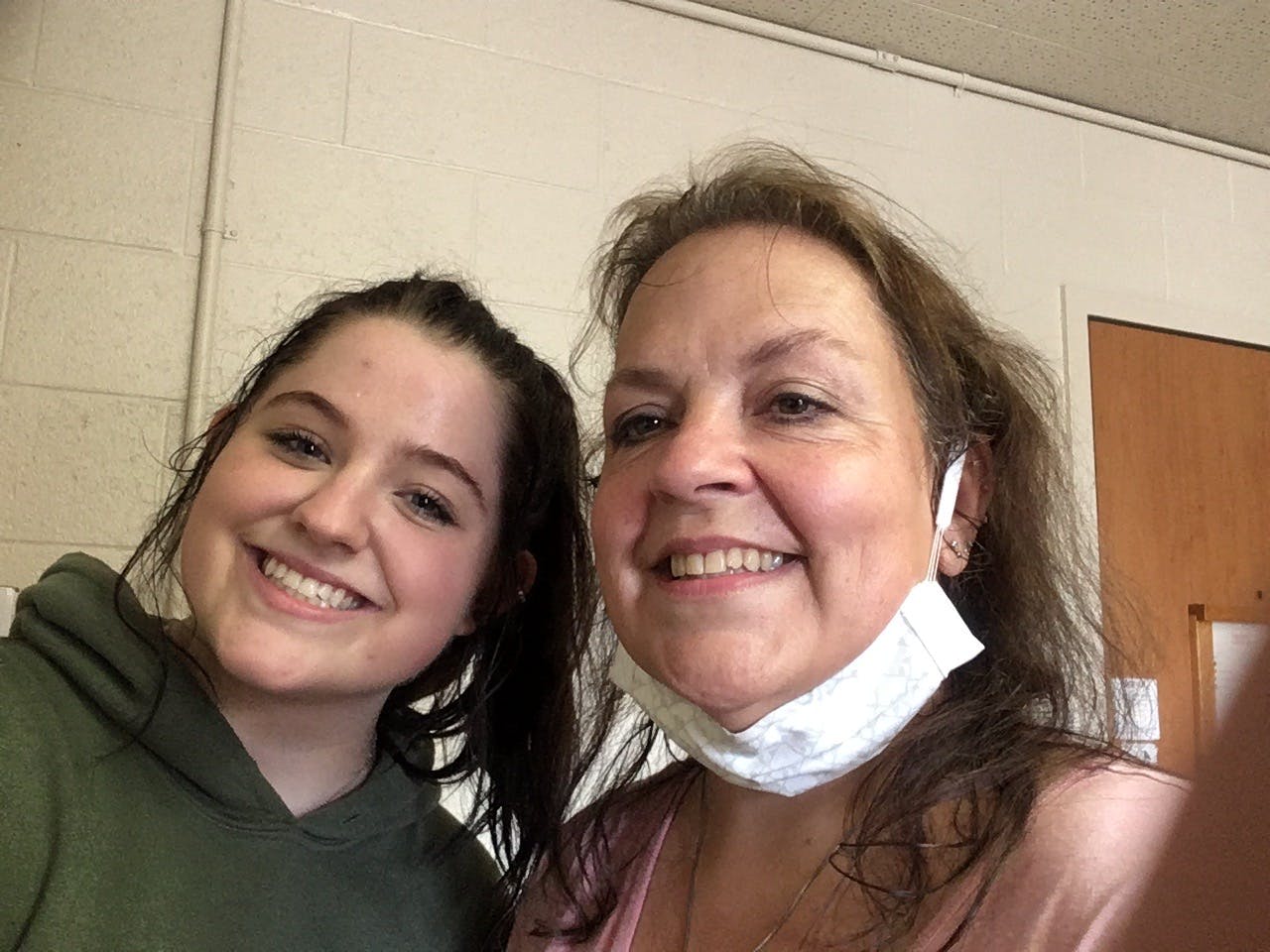 Two people smiling at the camera, one with a mask pulled down