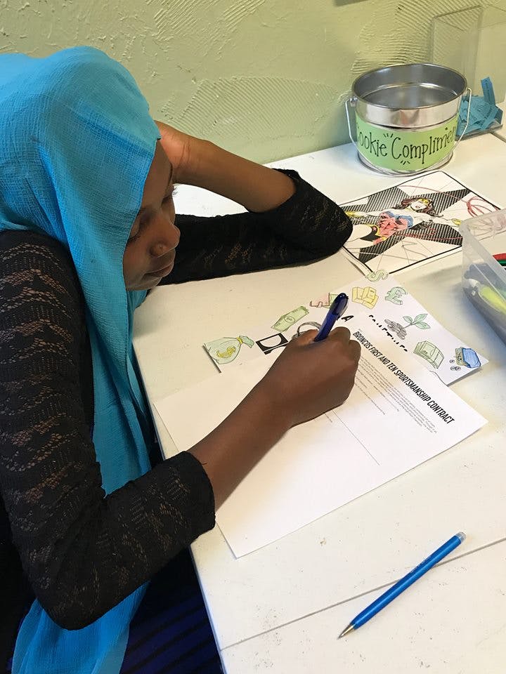 Person in a blue head covering writing on a document with a pen