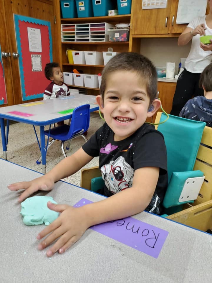 Child with hearing aids playing with light blue playdough at a table
