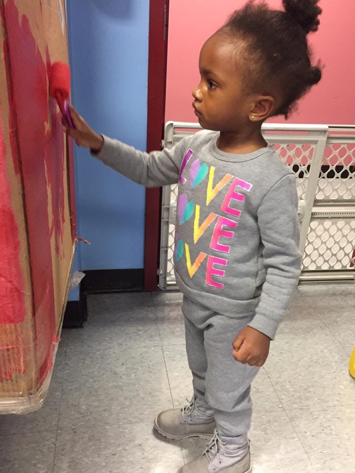 Child painting a cardboard box with a roller