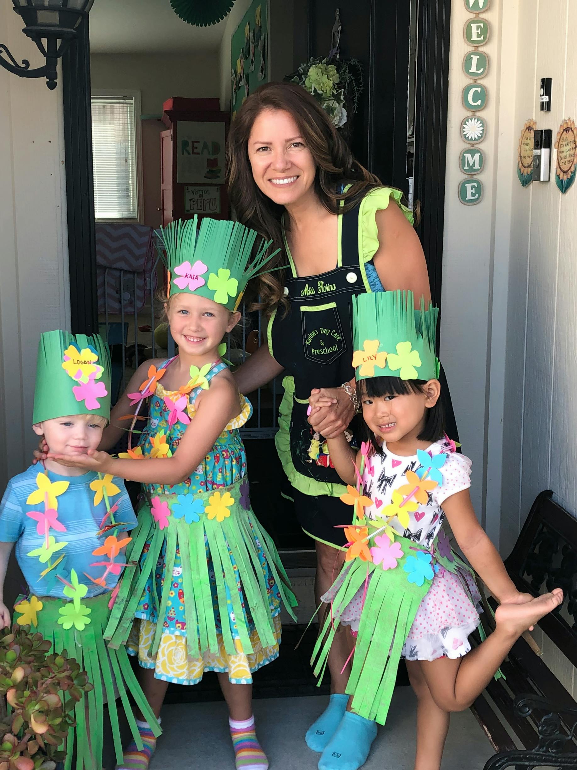 Adult and three children in green paper hats and grass skirts