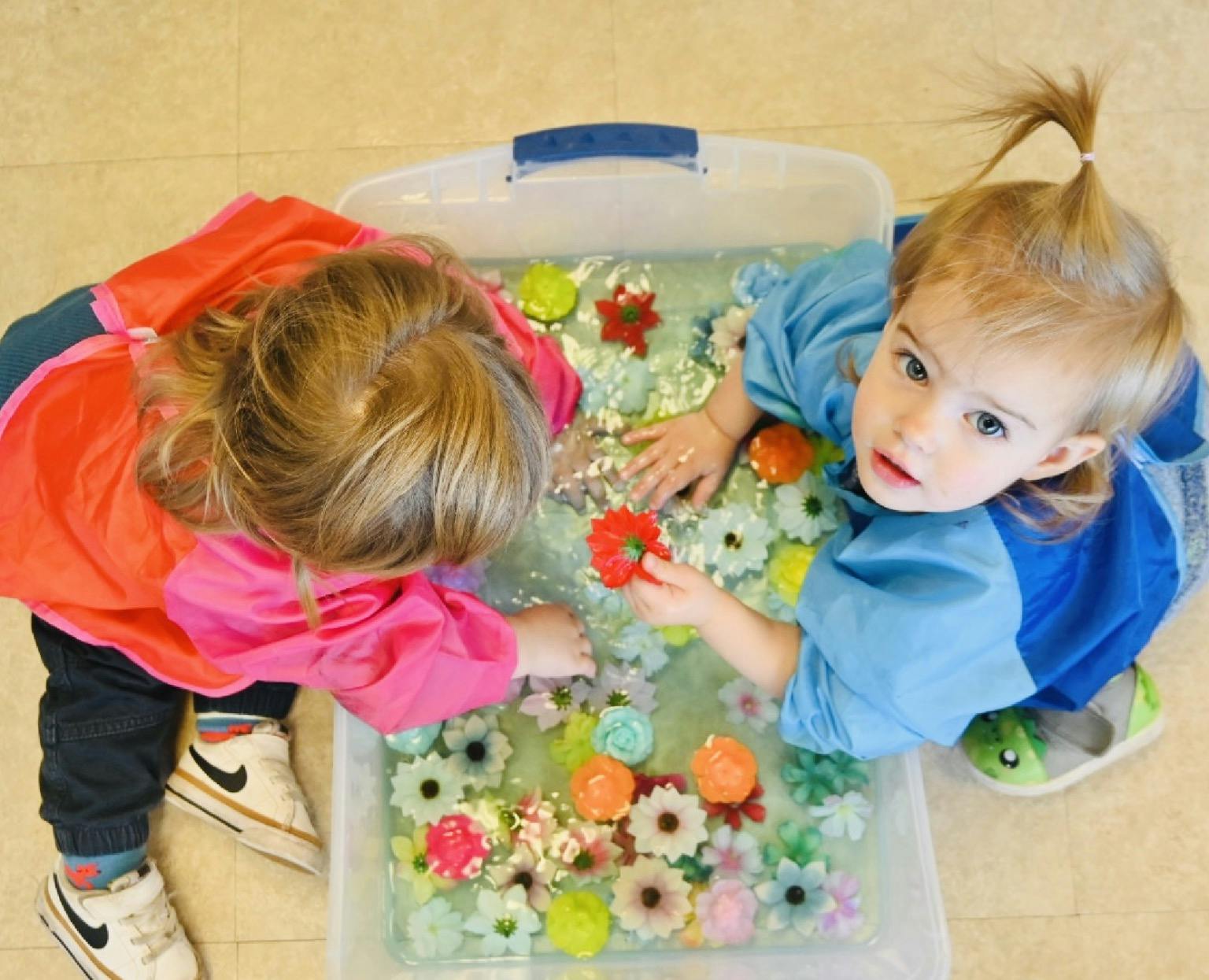 Two children playing with floating toy flowers in a water bin