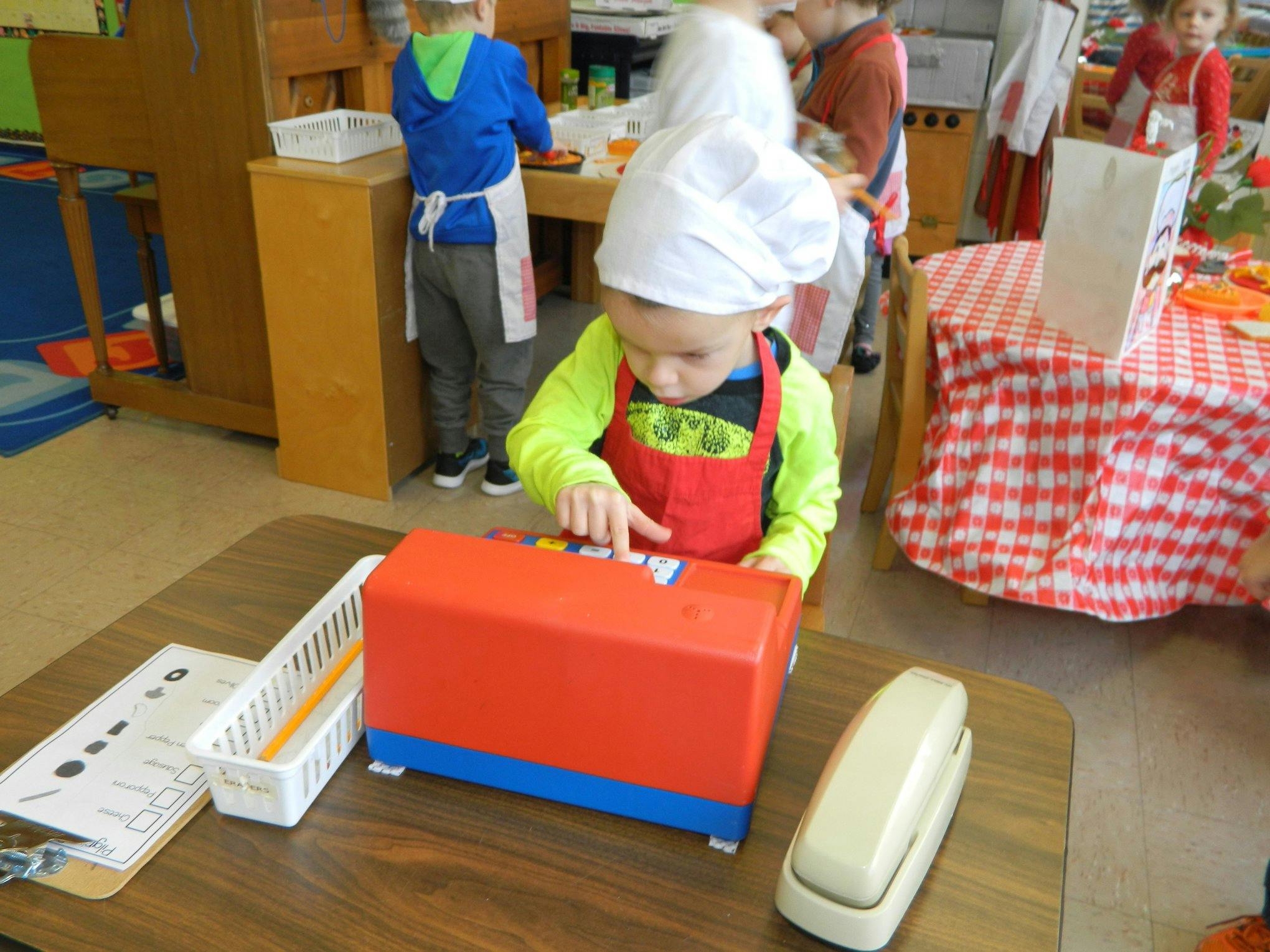 Child in chef hat and apron playing with a toy cash register