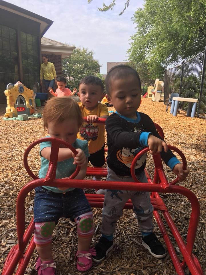 Three children playing on a red climbing structure outdoors