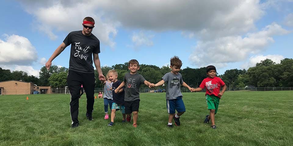 Person holding hands with four children walking across a grassy field