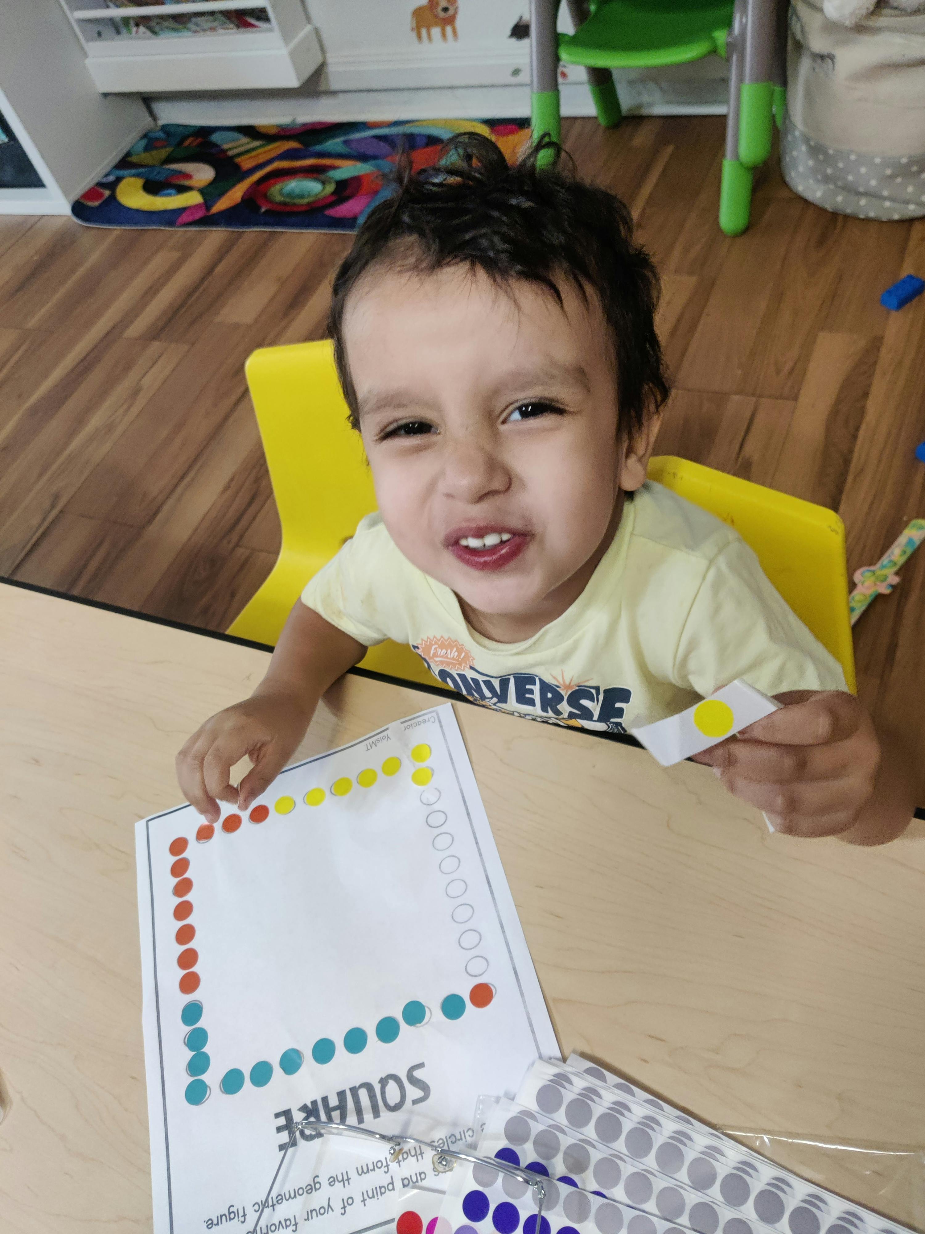 Child sitting at a table placing stickers on a paper square worksheet