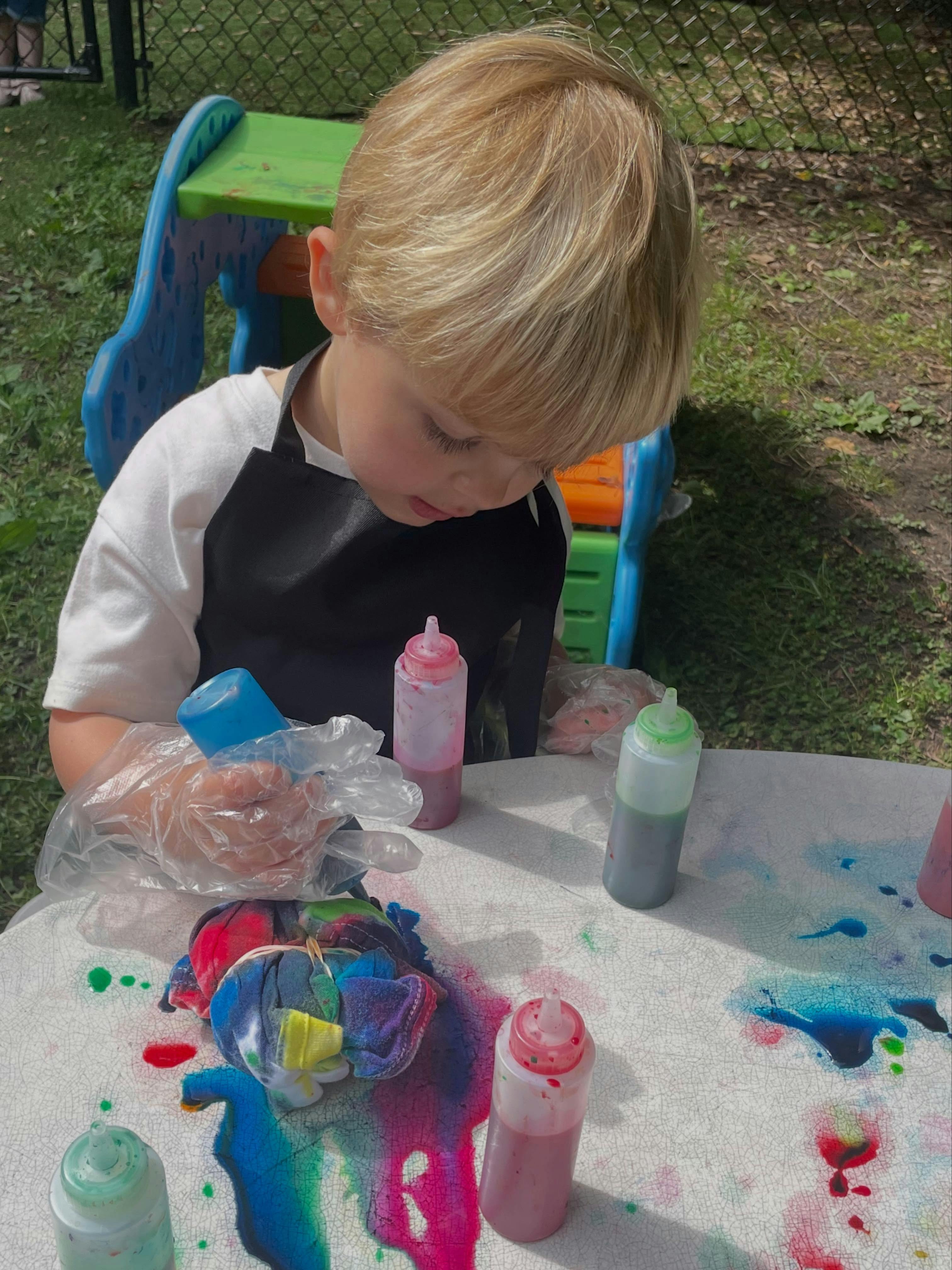 Child wearing an apron tie-dyeing a piece of fabric outdoors