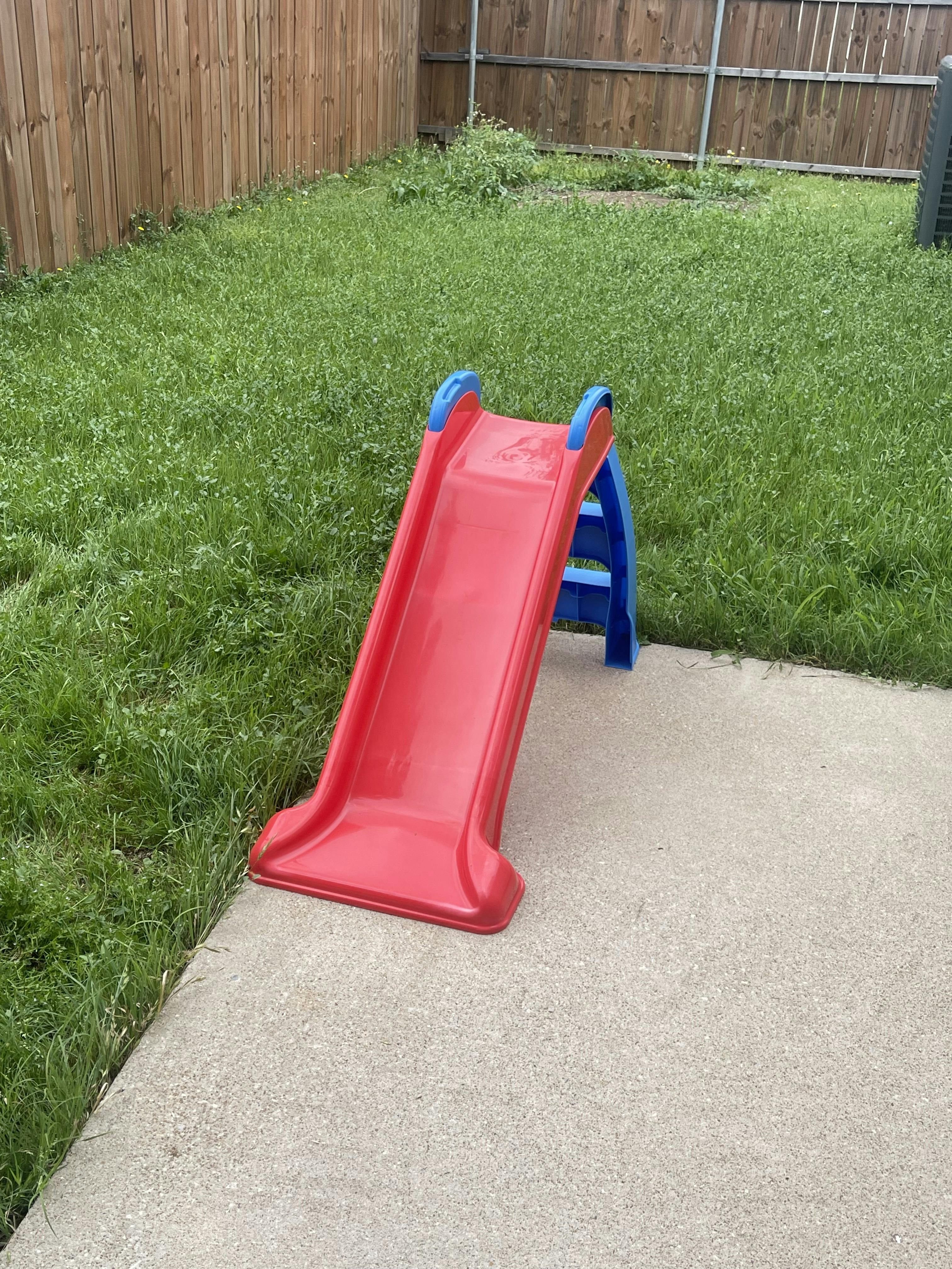 Red and blue child's slide on concrete next to grass