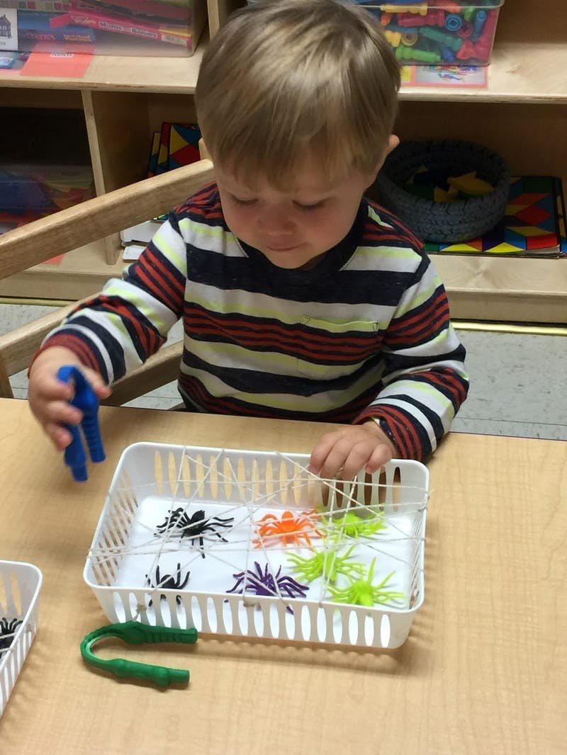 Child playing with plastic spiders and string in a basket