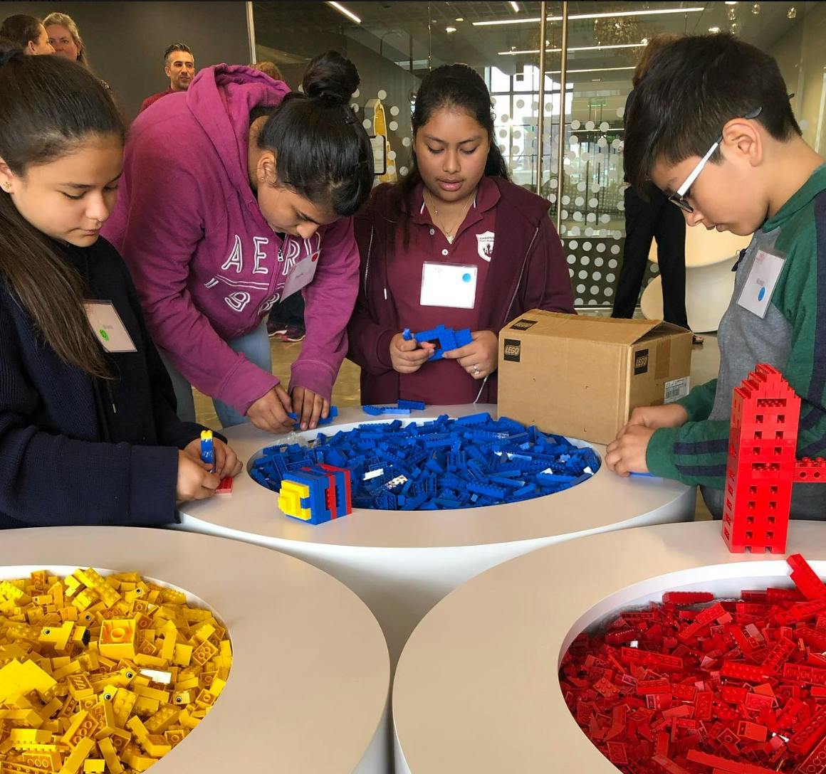 Four children building with blue, yellow, and red interlocking toy bricks