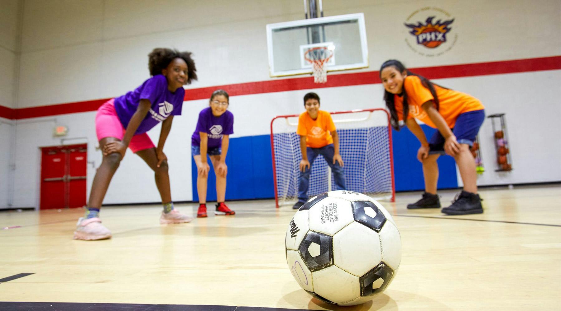 Four children in a gym with a soccer ball in the foreground