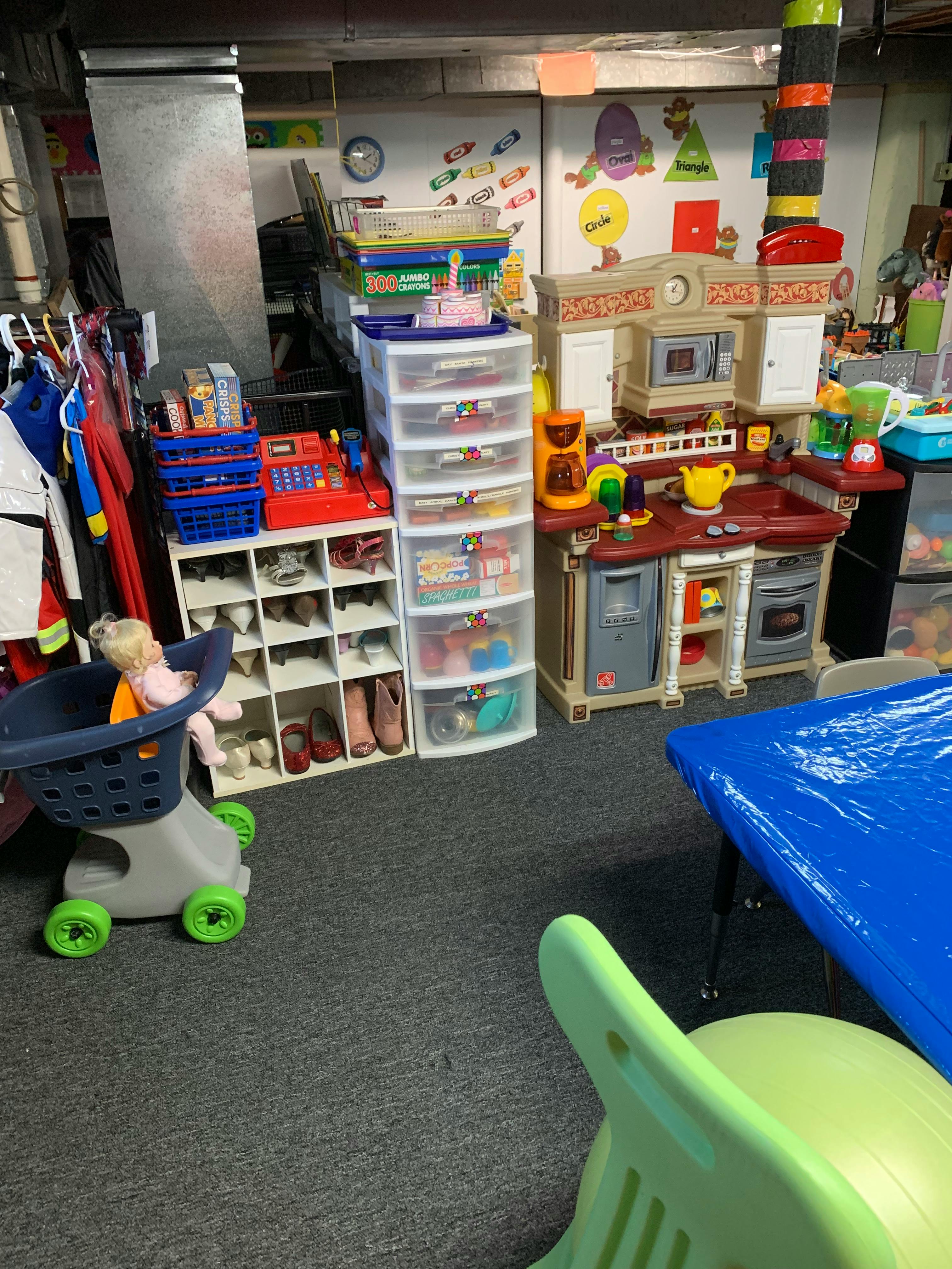 Doll in a toy shopping cart in a room with toys and storage