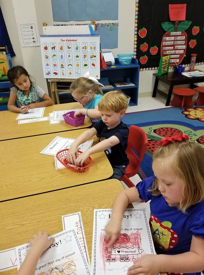 Children sitting at desks in a classroom, coloring and playing with items