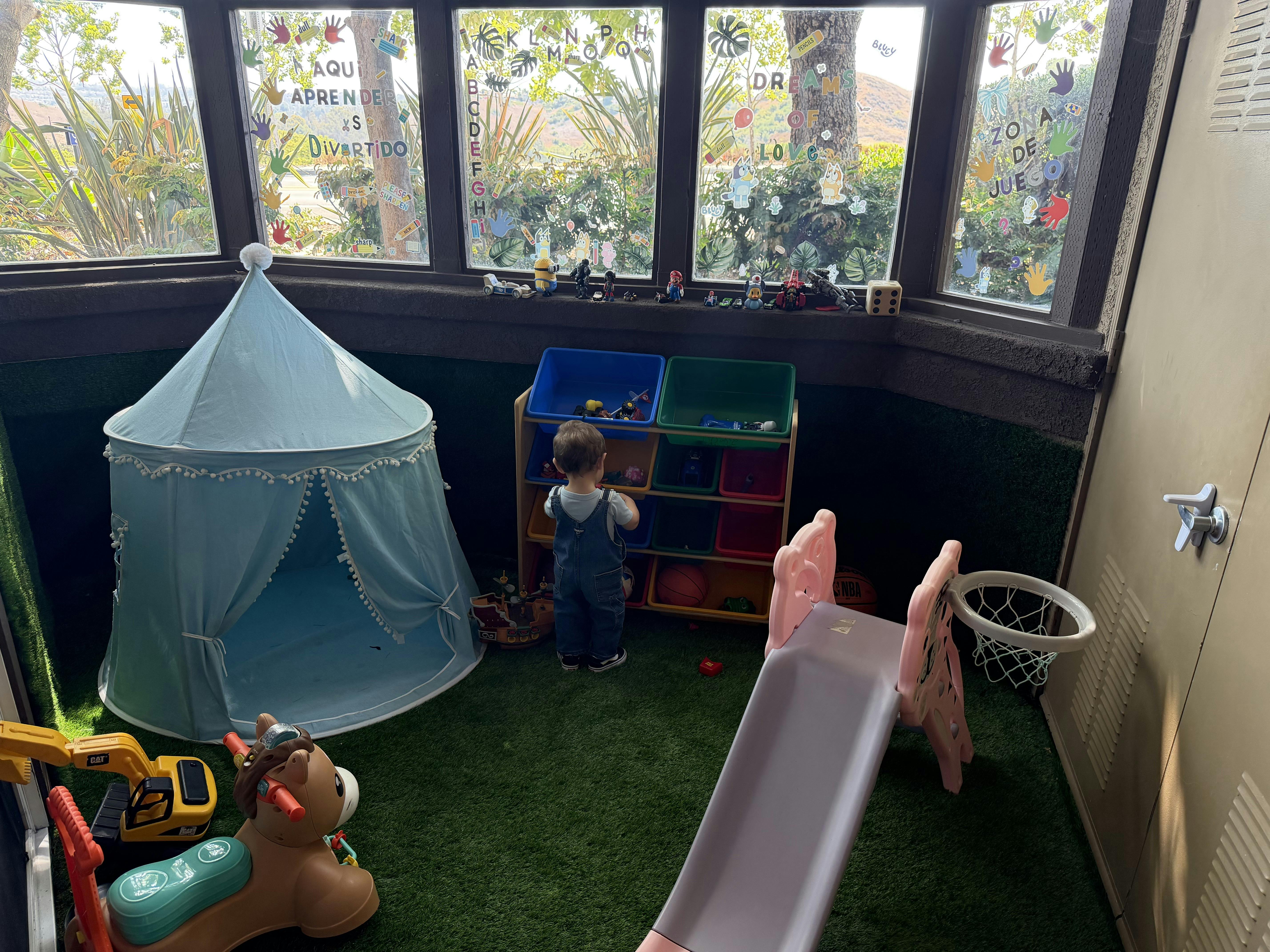 Child standing at a toy storage unit in a play area with a tent and slide