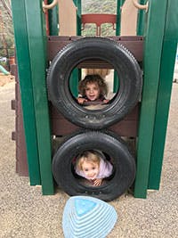 Two children looking through tires on a playground