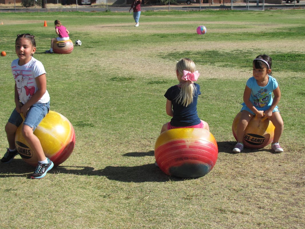 Three children sitting on bouncy balls on a grassy field