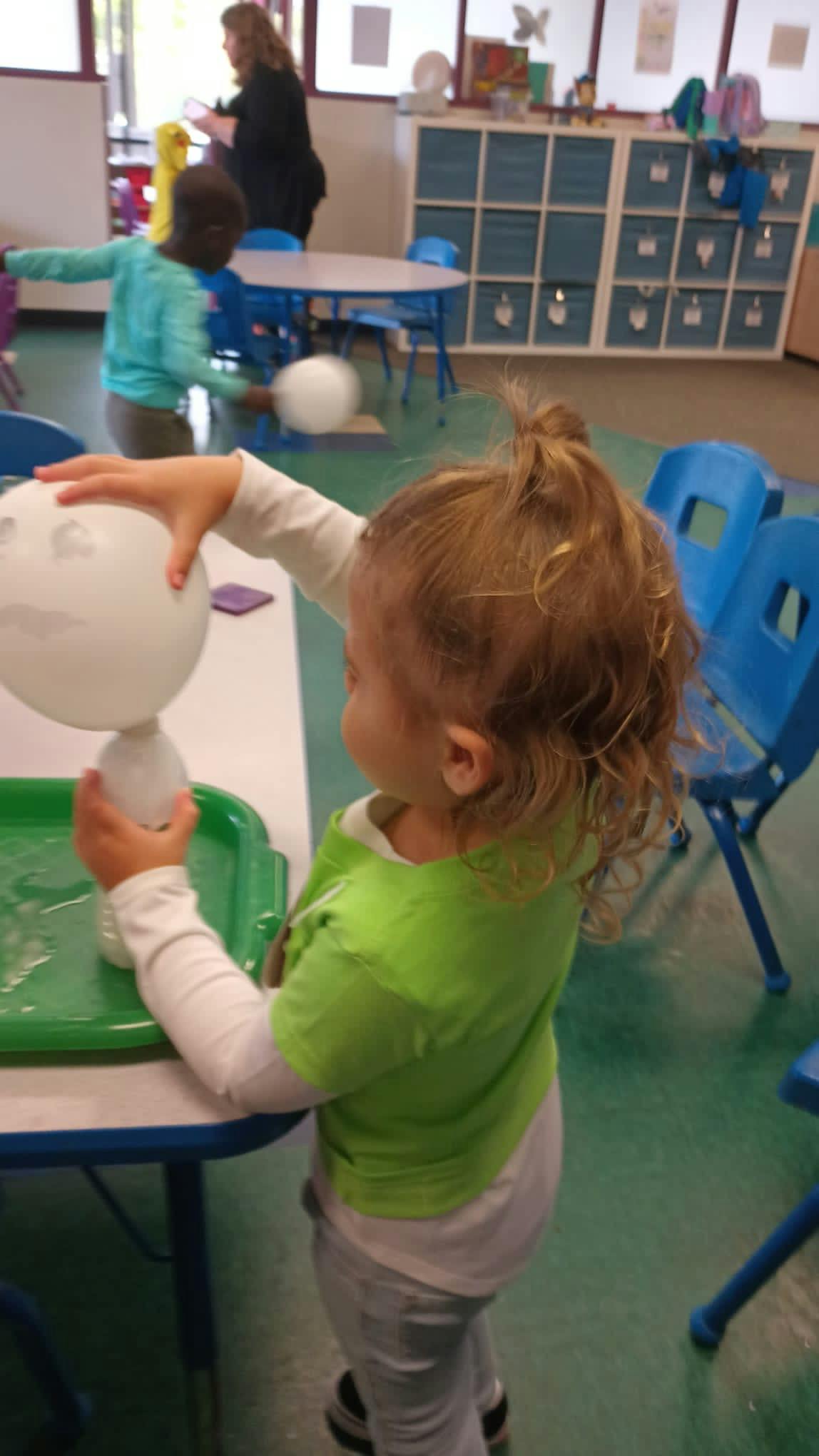 Child in a classroom touching a white balloon on a stand