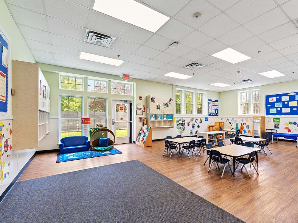 Classroom with small tables and chairs, and a blue couch and rug near a window