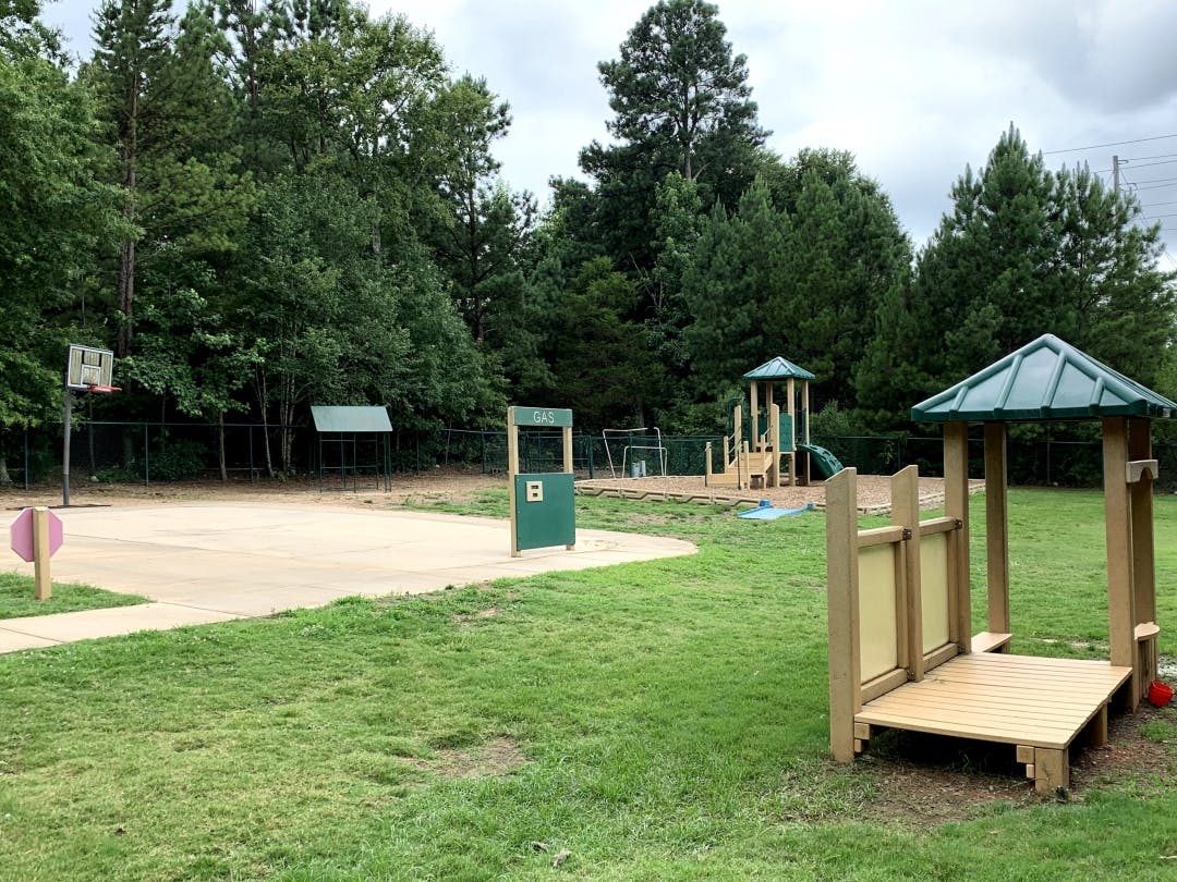 Basketball hoop on a court next to a wooden playground structure and green play gas pump