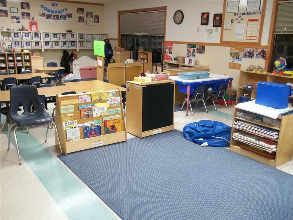 Classroom with tables, chairs, bookshelves, and a blue play mat