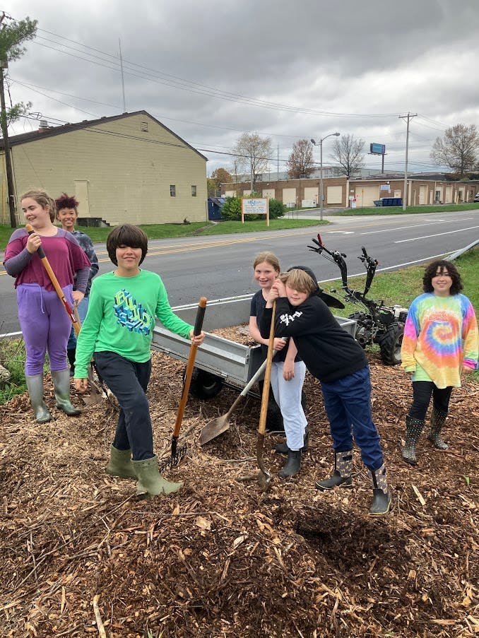 Group of children with shovels and rakes standing in wood chips