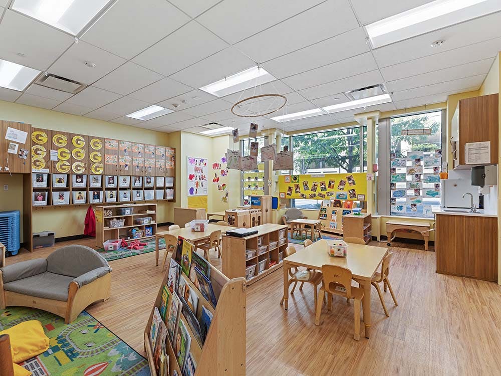 Empty classroom with small tables and chairs, shelves, and large windows