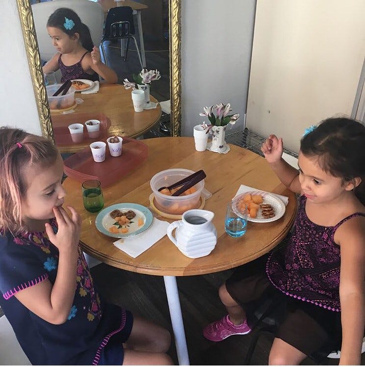 Two children sitting at a table with food and drinks
