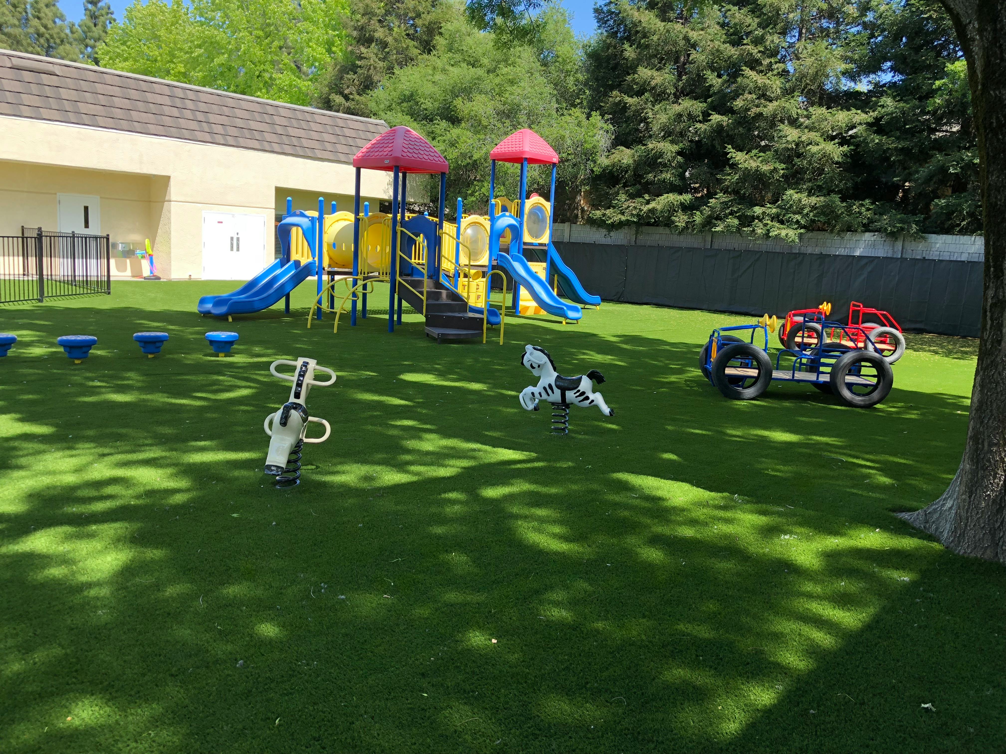 Playground with slides, climbing structure, and spring riders on artificial turf