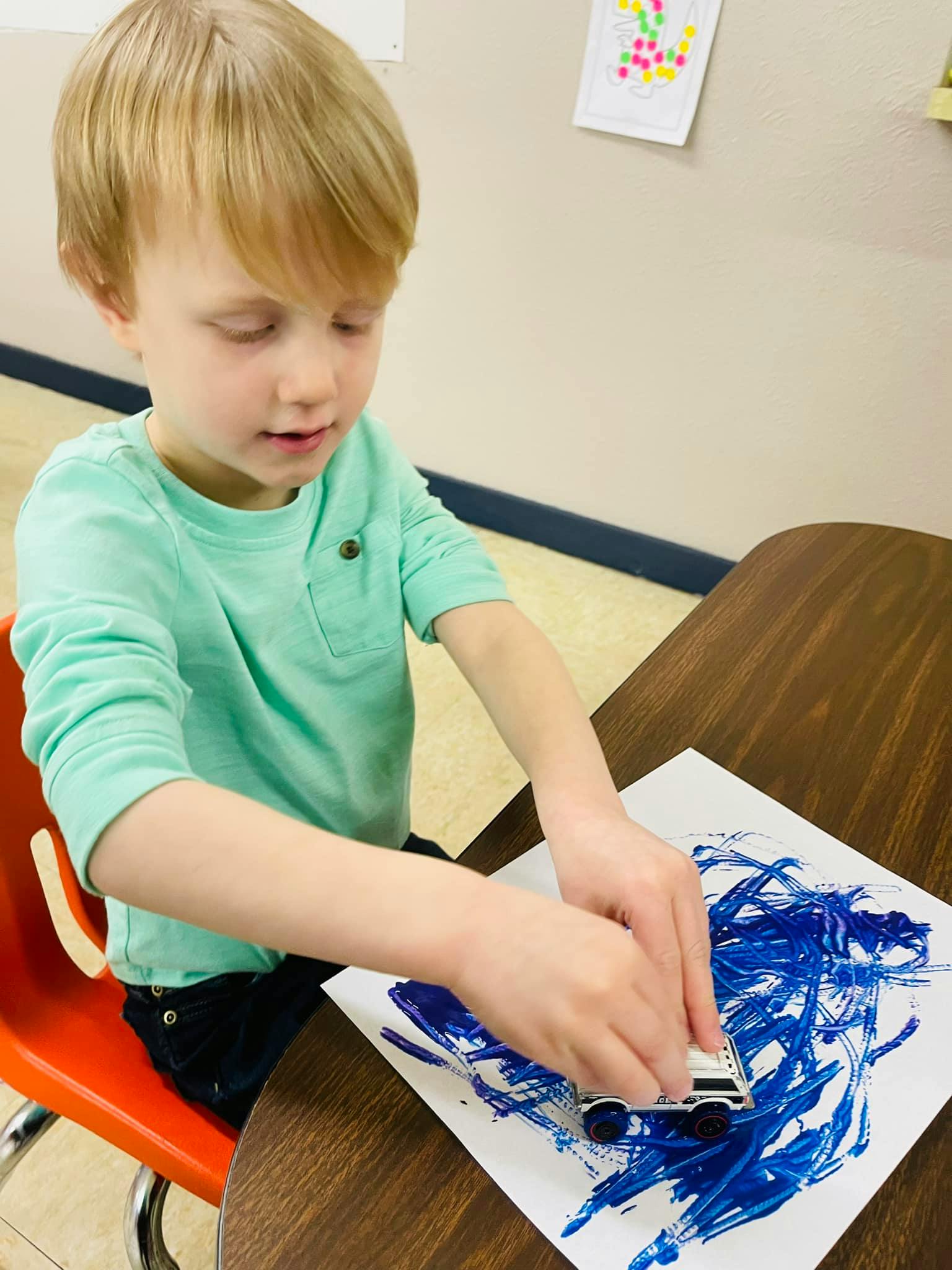 Child using a toy car to spread blue paint on paper