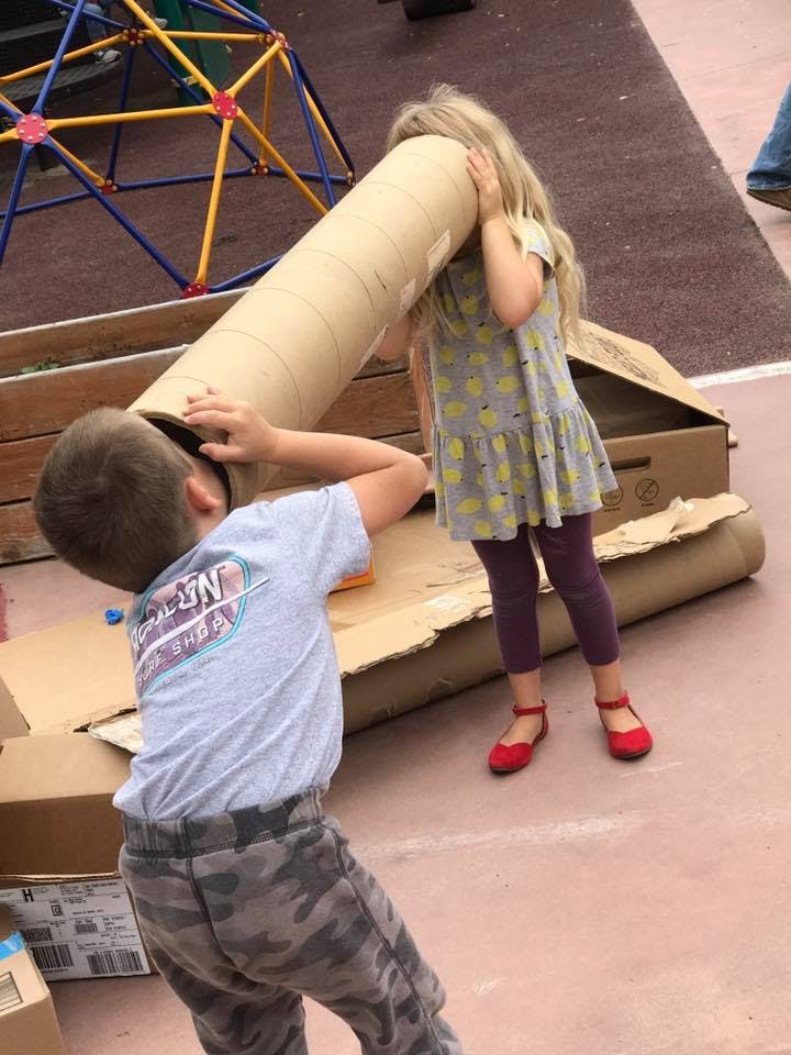 Two children playing with a large cardboard tube