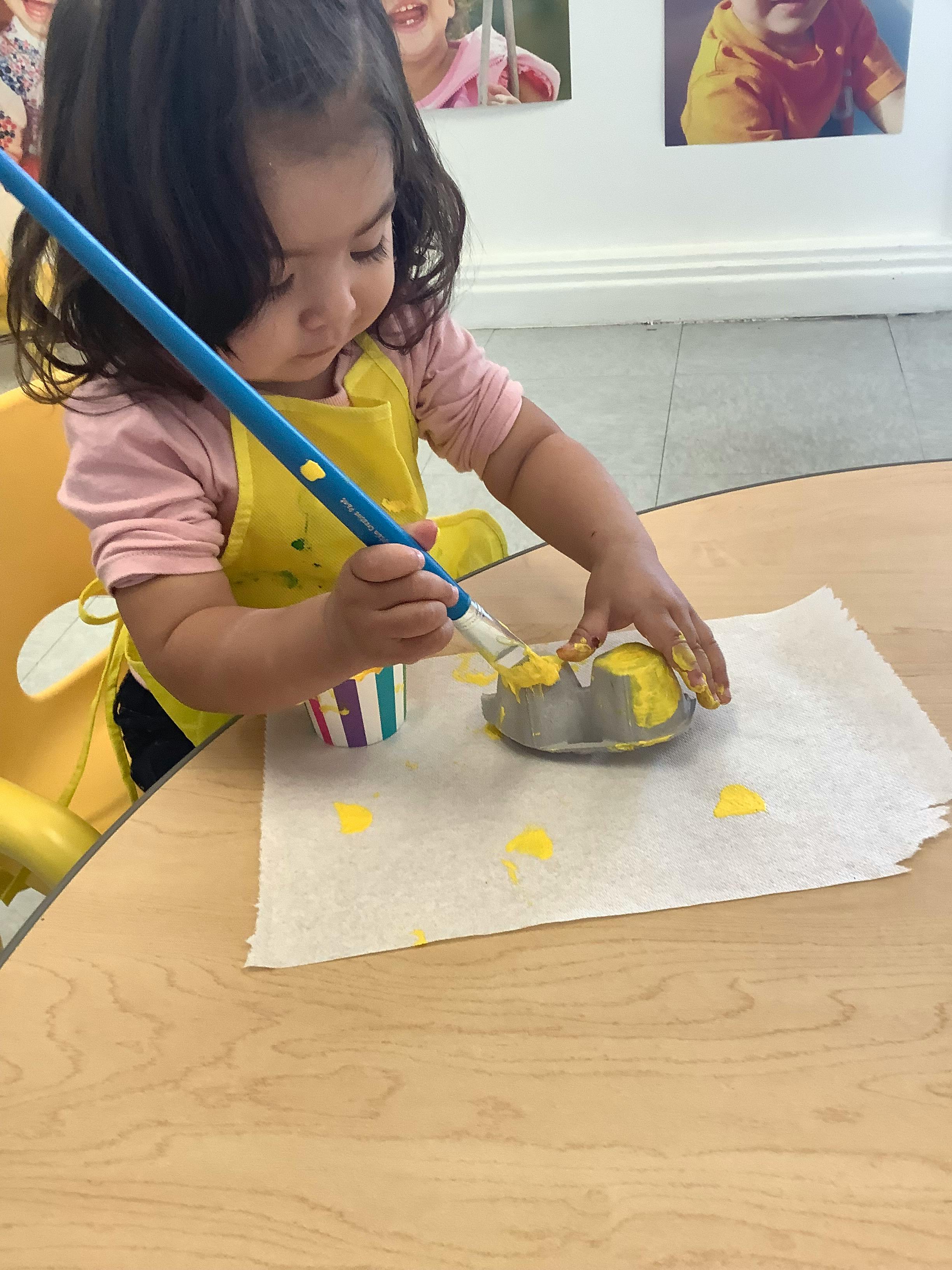 Child painting a craft with yellow paint at a table