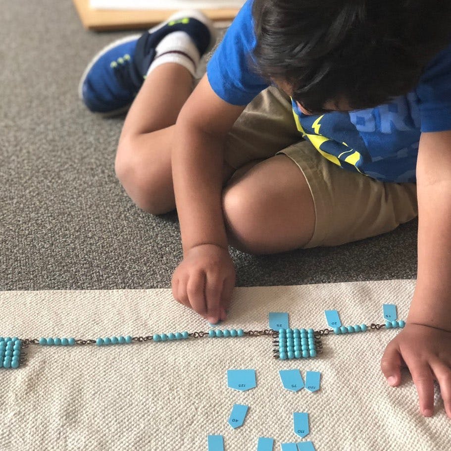 Child on floor playing with blue beads and tiles