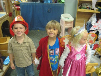 Three children in costumes, one in a firefighter hat, one in a red robe, one in a pink dress