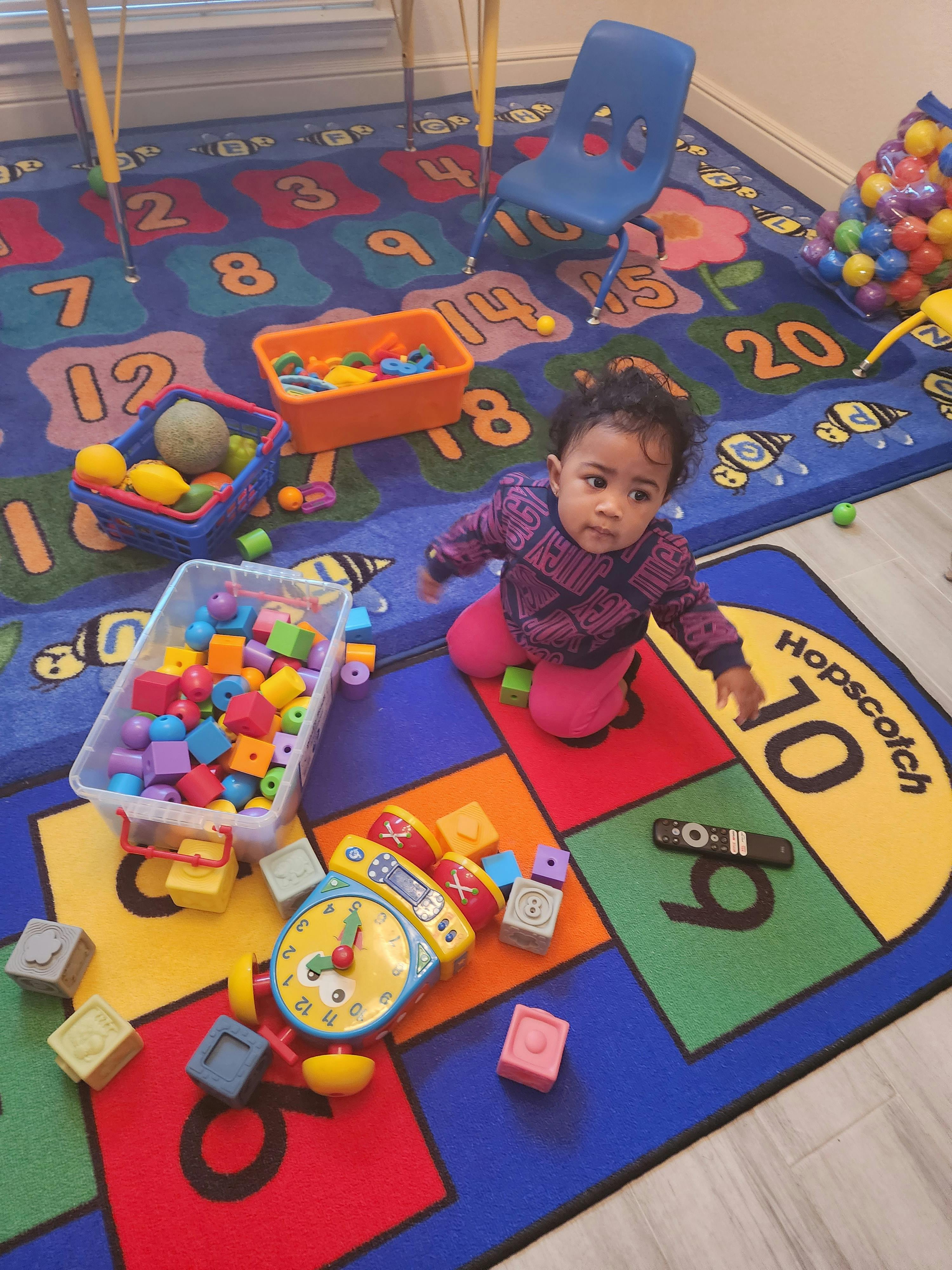 Child playing on a colorful rug with toys