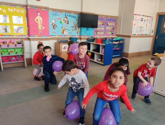 Children playing with purple balloons in a classroom